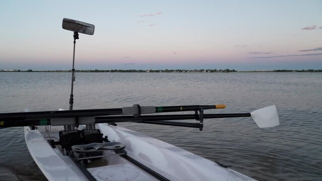 Rowing shell with hatchet oars, sliding seat and rowing mirror is wobbling in waves at dusk on a shore of Boyd Lake, Colorado