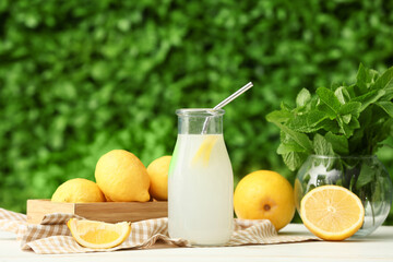 Bottle of fresh lemonade and vase with mint on white wooden table outdoors