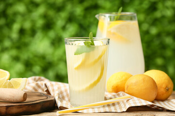 Glass and jug of fresh lemonade with mint on wooden table outdoors