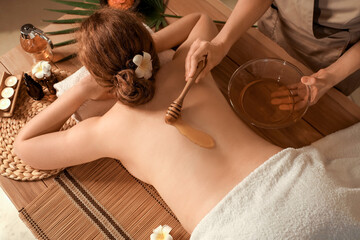 Massage therapist pouring honey on woman's back in dark spa salon, top view