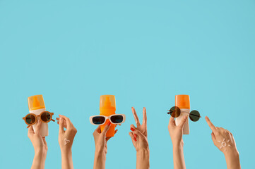 Female hands holding sunscreen creams with sunglasses on blue background