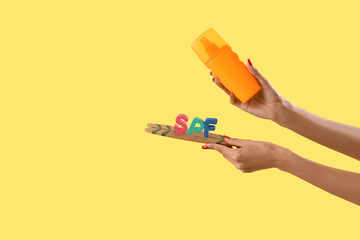Female hands with sunscreen cream and letters SPF on mini surfboard on yellow background