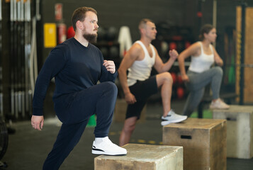 Sportive young man doing step-up exercises with box in gym during training session