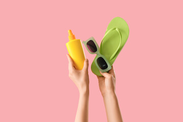 Female hands with flip-flop, sunscreen cream and sunglasses on pink background