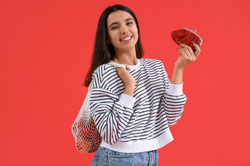 Young woman with wallet and string shopping bag on red background