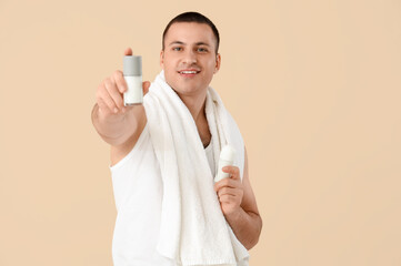 Handsome young man applying deodorants on beige background