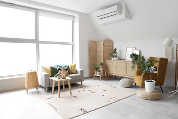 Interior of light living room with grey sofa, armchair and drawers