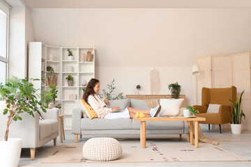 Young Asian woman using laptop on sofa at home