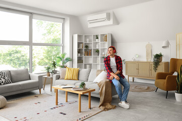 Fototapeta premium Young man in headphones sitting on sofa at home