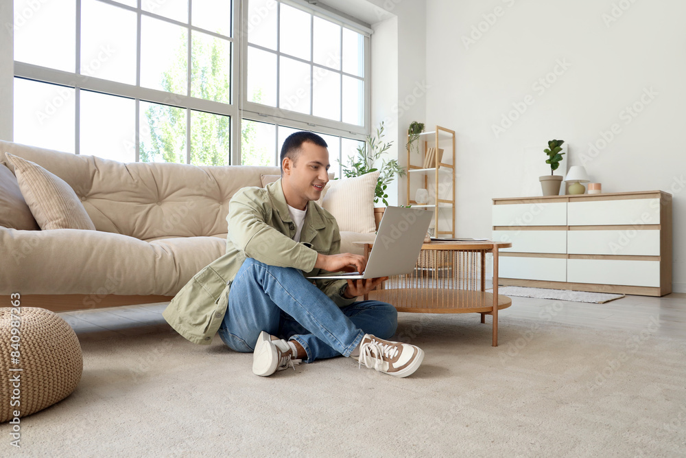 Wall mural Young man using laptop on soft carpet at home