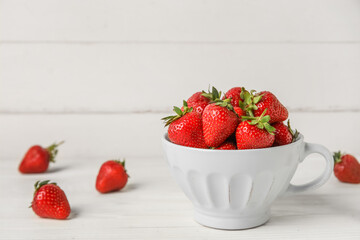 Cup with sweet fresh strawberries on white wooden background