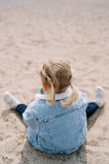 Little girl sits with a toy on the sand. Back view