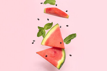 Flying pieces of fresh watermelon with mint and seeds on pink background