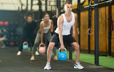 Concentrated athletic young man participating in intense group training in modern gym, doing exercises with kettlebells. Fitness and bodybuilding concept..