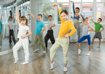 Fototapeta premium Dynamic little girl training Rock-and-Roll dance poses with instructor and other attendees of dancing courses