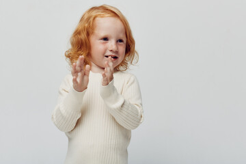 Redhaired little girl with hands raised in front of white background, joyful and carefree expression, childhood innocence and beauty
