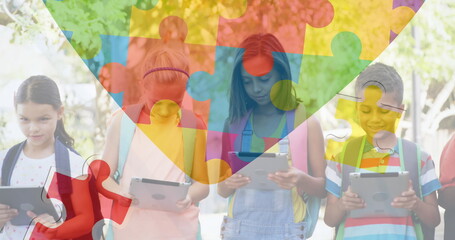 Image of colourful puzzle pieces and heart over kids friends using electronic devices