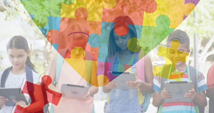 Image of colourful puzzle pieces and heart over kids friends using electronic devices