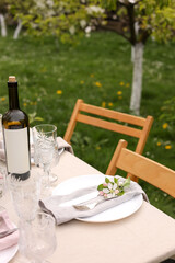 Stylish table setting with beautiful spring flowers, wine, plates and glasses in garden