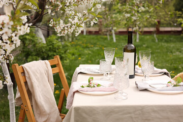 Stylish table setting with beautiful spring flowers, wine, plates and glasses in garden