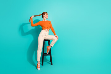 Full size photo of satisfied girl dressed orange shirt pants sitting on stool hold tail look empty...