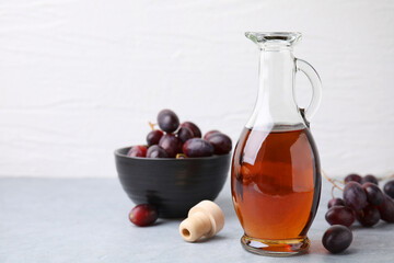 Wine vinegar in glass jug and grapes on grey table, space for text