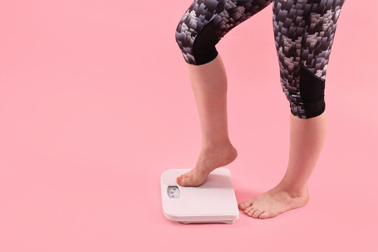 Woman stepping on floor scale against pink background, closeup. Space for text