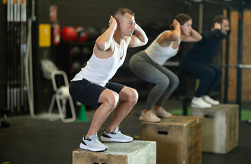 Active young guy squatting on box in sports hall during crossfit workout