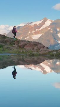 A hiker walks on a rocky path by an alpine lake with snowcapped mountains in the background, radiating tranquility. Ideal for nature lovers seeking peaceful retreats in the wilderness