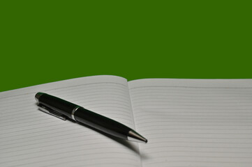 Shiny black pen and note book isolated shot with green plain background