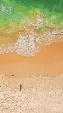 Vertical Screen: The video captures a person peacefully walking on a sandy beach with vibrant waves, perfect for relaxation. Ideal for those seeking a tranquil coastal escape and travel enthusiasts