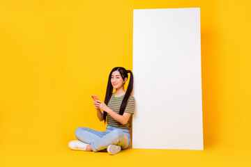Photo of young lovely teen schoolgirl sit near big smartphone board panel isolated on yellow color...