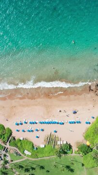 Vertical Screen: Relax and unwind at a serene beach with turquoise waters, blue umbrellas, lush greenery, and a panoramic view. Ideal tropical getaway for a peaceful vacation by the ocean