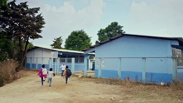 Children come running happily to school to receive classes and the teacher welcomes them happily.