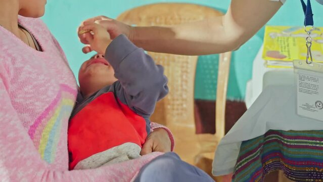 Child resists receiving the drinkable vaccine that the nurse wants to administer.