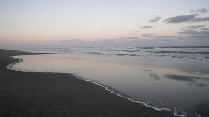 Panorama view of the ocean waves and beach under a sunset sky. The landscape reflection in the water.