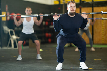 Determined young guy working out with weight rod in gym during training session