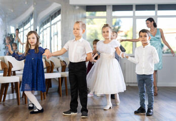 Merry junior schoolchildren in party dresses lined up in pairs during waltz dance in social hall