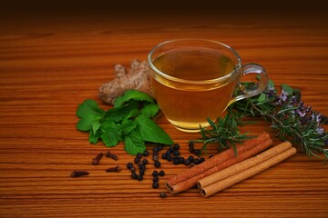 cup of herbal tea, medicinal drink, immunity booster with ingredients, ginger, cinnamon, Tulsi, holy basil leaves, black peppercorns, mint leaves, rosemary, cloves on a table