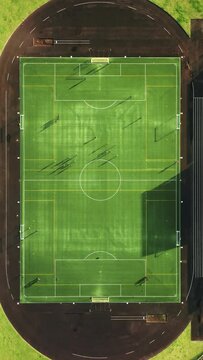 Vertical Screen: An overhead view captures a football field with players in training. Sunlit shadows on the turf form a lively pattern, portraying a dynamic practice session in the stadium