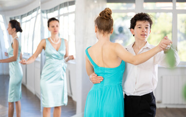 Girl and a boy in festive clothes learn to dance tango under guidance of a teacher