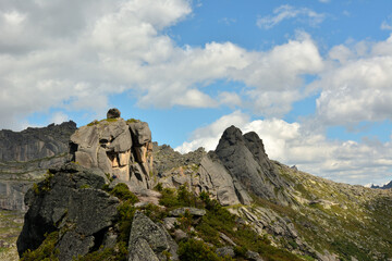 Pointed rocks of a mountain range with a round stone on top under a cloudy clear sky.