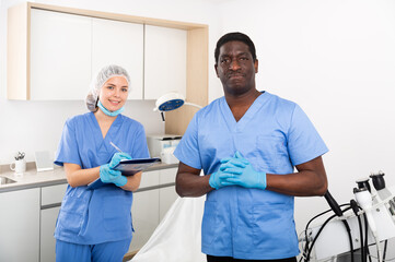 Obraz premium Two professional cosmetologists meeting patient in medical office, female doctor filling out medical form at clipboard