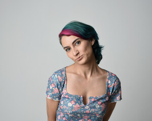 a close up head and shoulders portrait of young alternative female model, with pink and grey shaved undercut hair style, wearing a floral blue top. dramatically pulling expressive facial expressions. 
