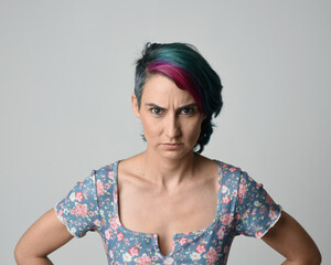 a close up head and shoulders portrait of young alternative female model, with pink and grey shaved undercut hair style, wearing a floral blue top. dramatically pulling expressive facial expressions. 