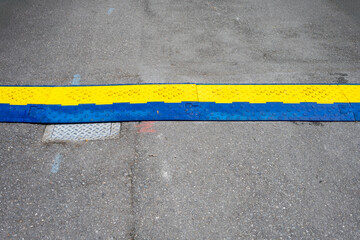 Blue and yellow heavy duty plastic cover protecting electrical cable crossing over an asphalt...