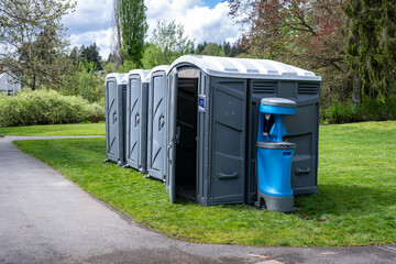 Setting up for a spring festival in a grass field in the park, portable bathrooms, including wheelchair accessible option, with a handwashing and sanitation station, sunny day outside
