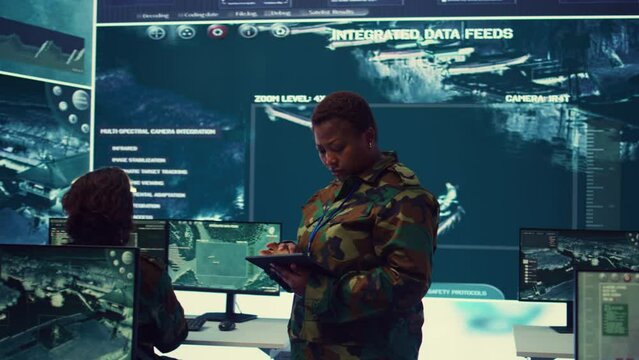 Woman high tech specialist studying satellite CCTV visualization on a big screen, preparing troops with insight for a new national safety mission. Female first lieutenant in command post. Camera B.