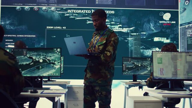 Military sergeant targeting enemy vessels on a gps satellite world map, operating from army power base monitoring room. Officer studies defense tactics on a tablet, command center. Camera B.