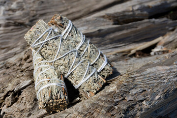 An image of three white small white sage smudge sticks stacked on a driftwood log. 
